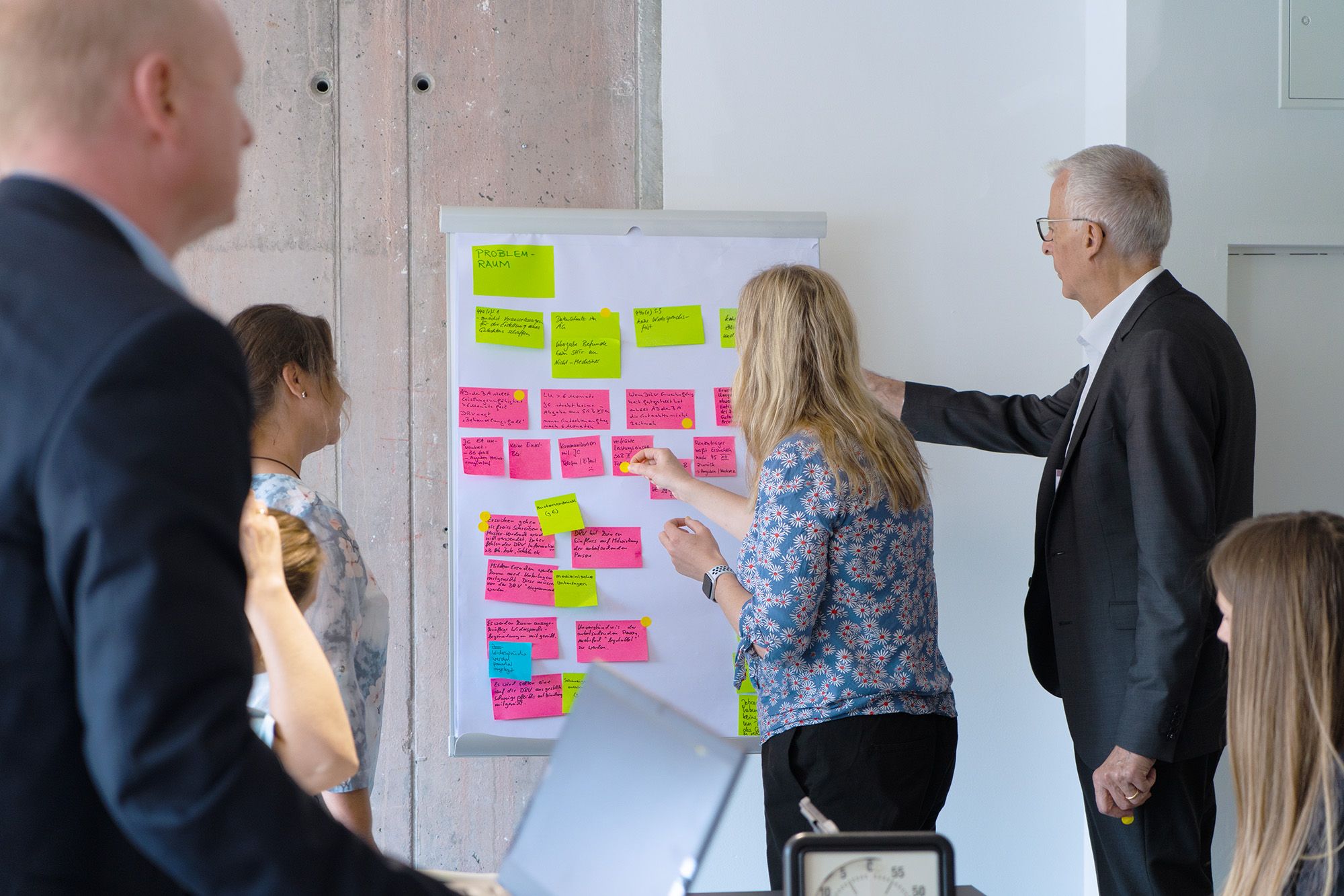 Teilnehmende eines Workshops kleben bunte Notizzettel an ein Whiteboard und diskutieren die Inhalte