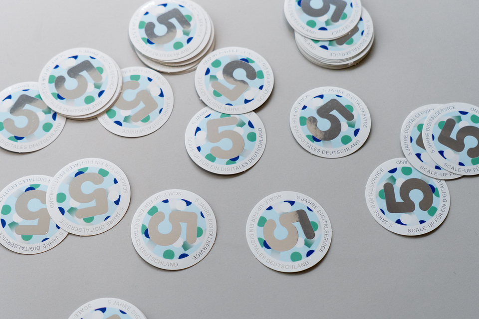 Mehrere Sticker mit einer großen Fünf in der Mitte liegen auf einem Tisch verteilt