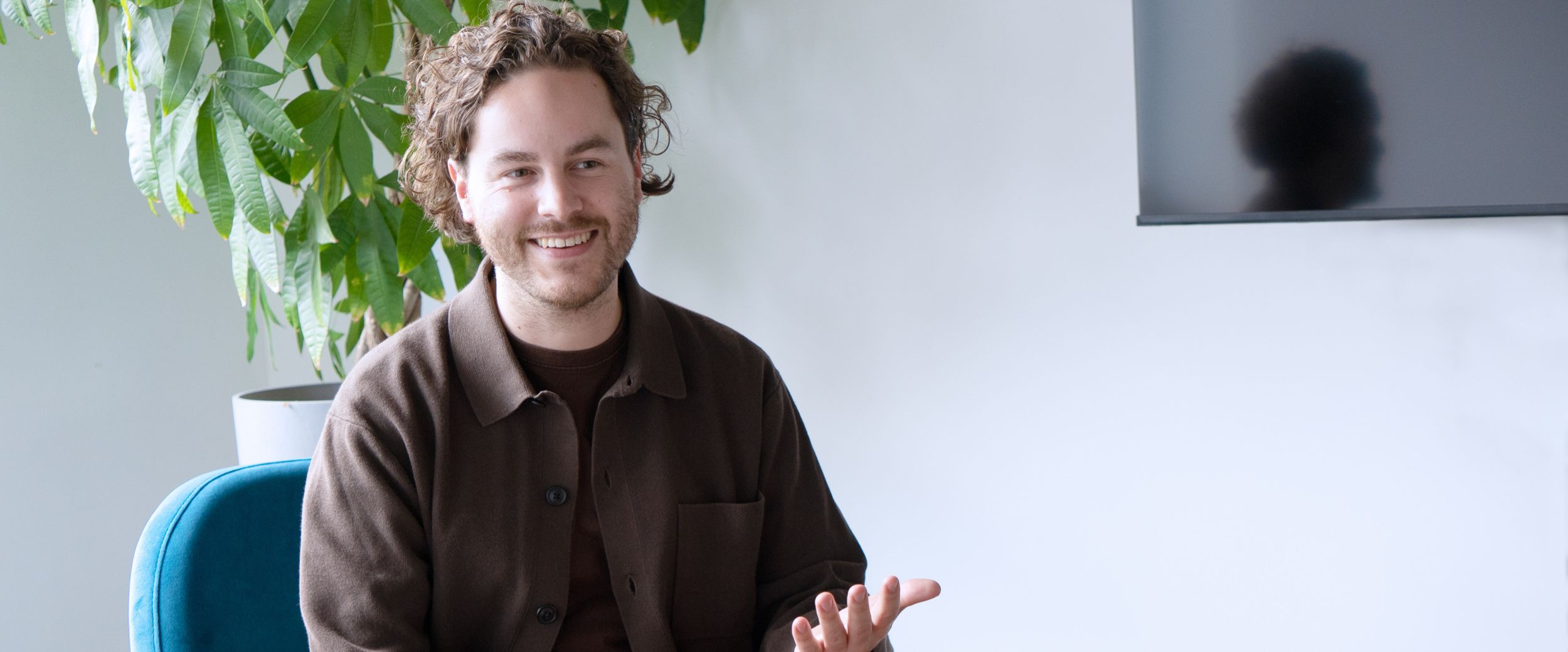 Joshua sitzt in einem modernen Büroraum, spricht und gestikuliert mit der Hand.