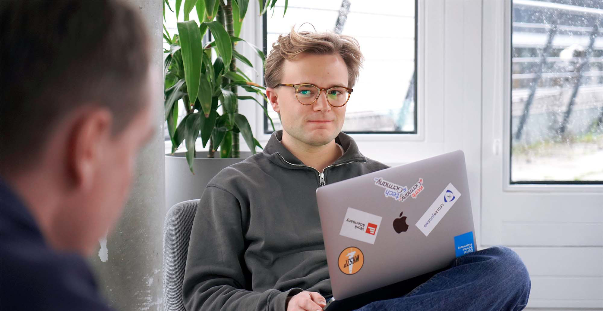 Interviewpartner Moritz hat sein Laptop auf den Beinen und sitzt im Büro des DigitalService, während er mit einem Kollegen spricht