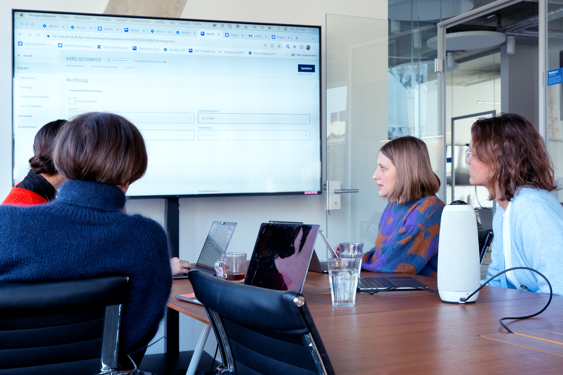 Vier Mitglieder des NeuRIS Projektteams diskutieren gemeinsam die Benutzeroberfläche des Online-Tools, das auf einem großen Bildschirm während eines Konzept-Testings zu sehen ist