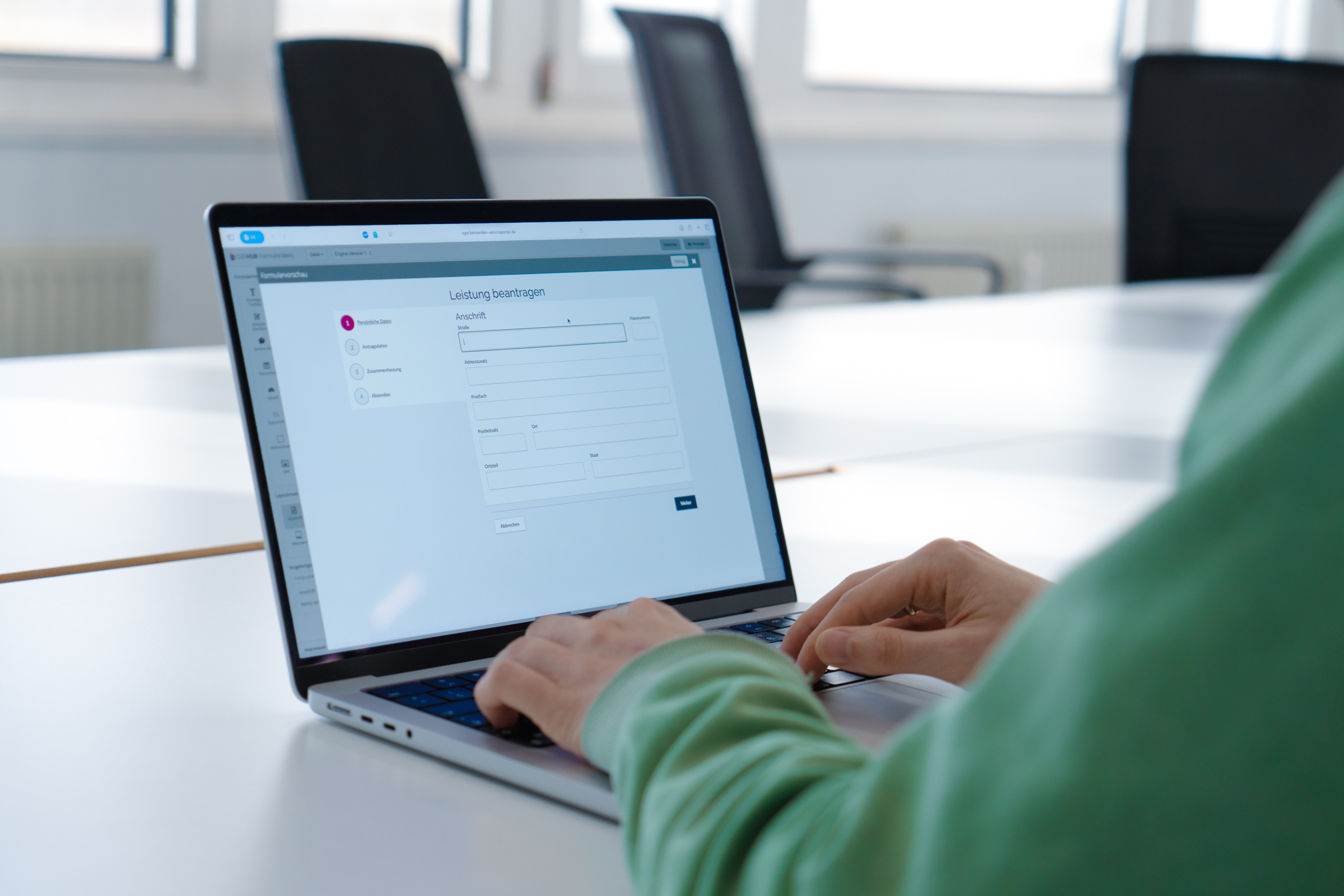 Eine Person sitz an einem Laptop auf dessen Bildschirm ein Formular zu sehen ist mit dem Titel „Leistung beantragen“