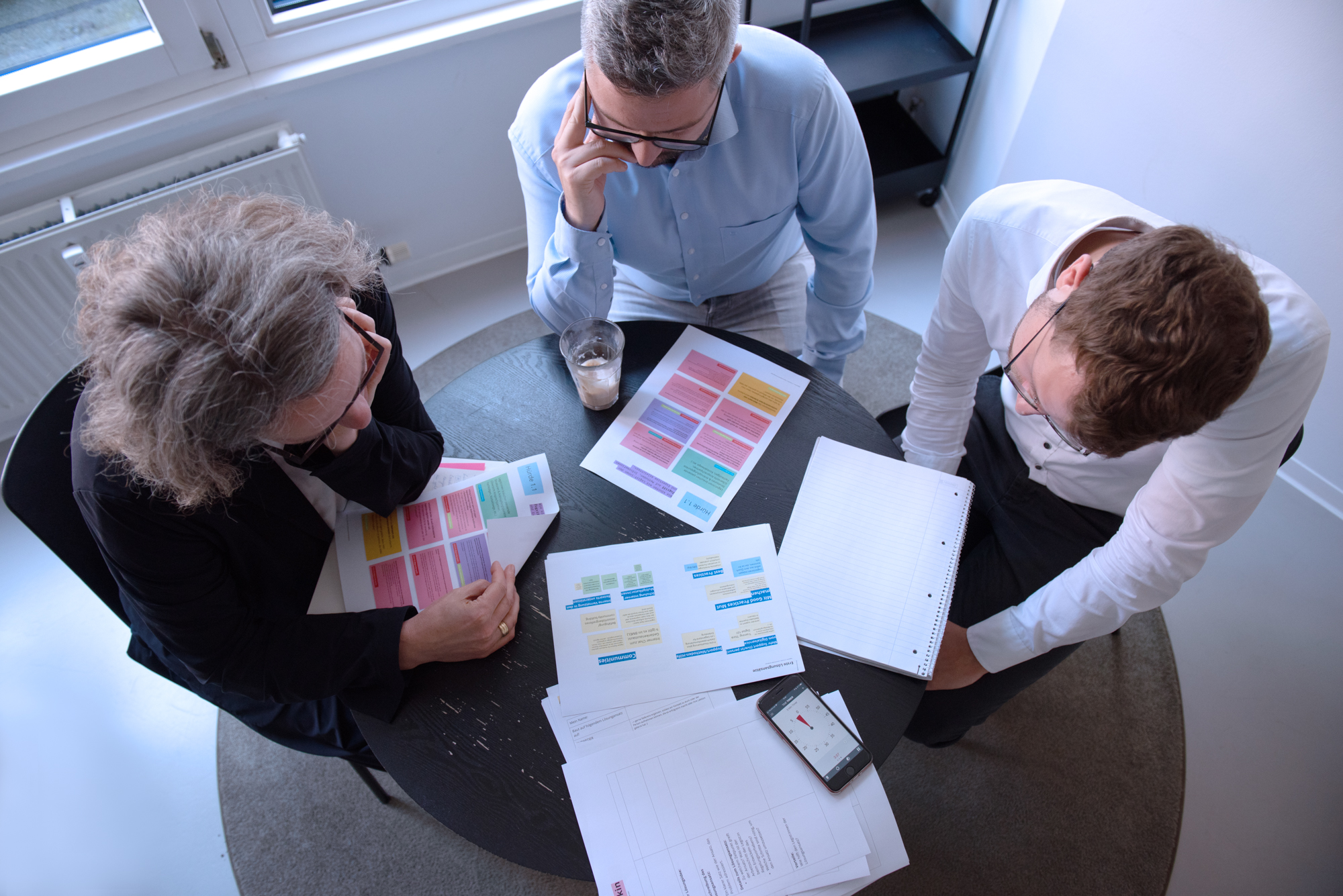 Drei Menschen beugen sich über einen Tisch und beraten sich über unterschiedliche Ausdrucke und Notizen.