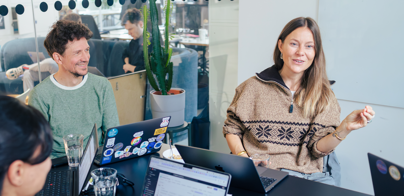 Mitarbeitende des DigitalService sitzen mit ihrem Laptops vor sich auf einem Tisch in einem Meetingraum und diskutieren gut gelaunt und lebhaft miteinander