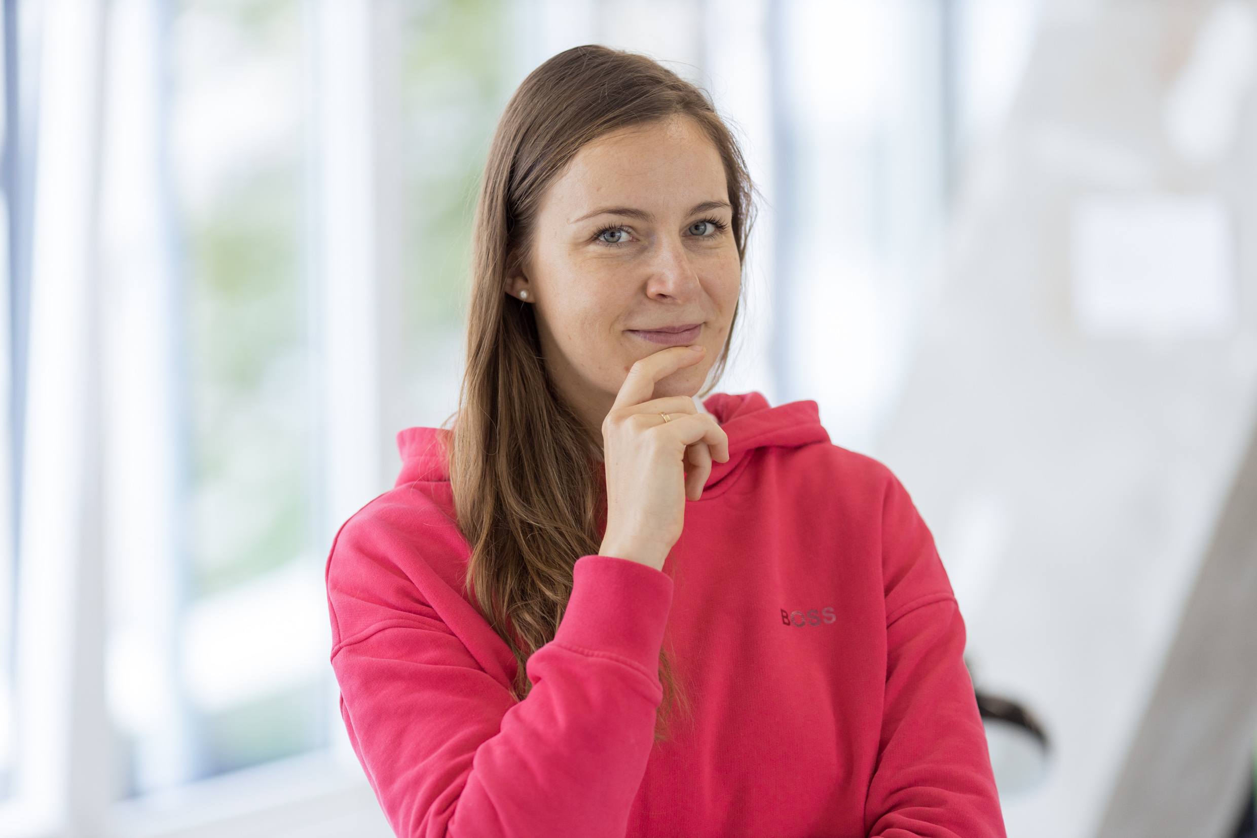 Compliance Managerin Julie in einem pinken Kapuzenpullover in Denkerpose
