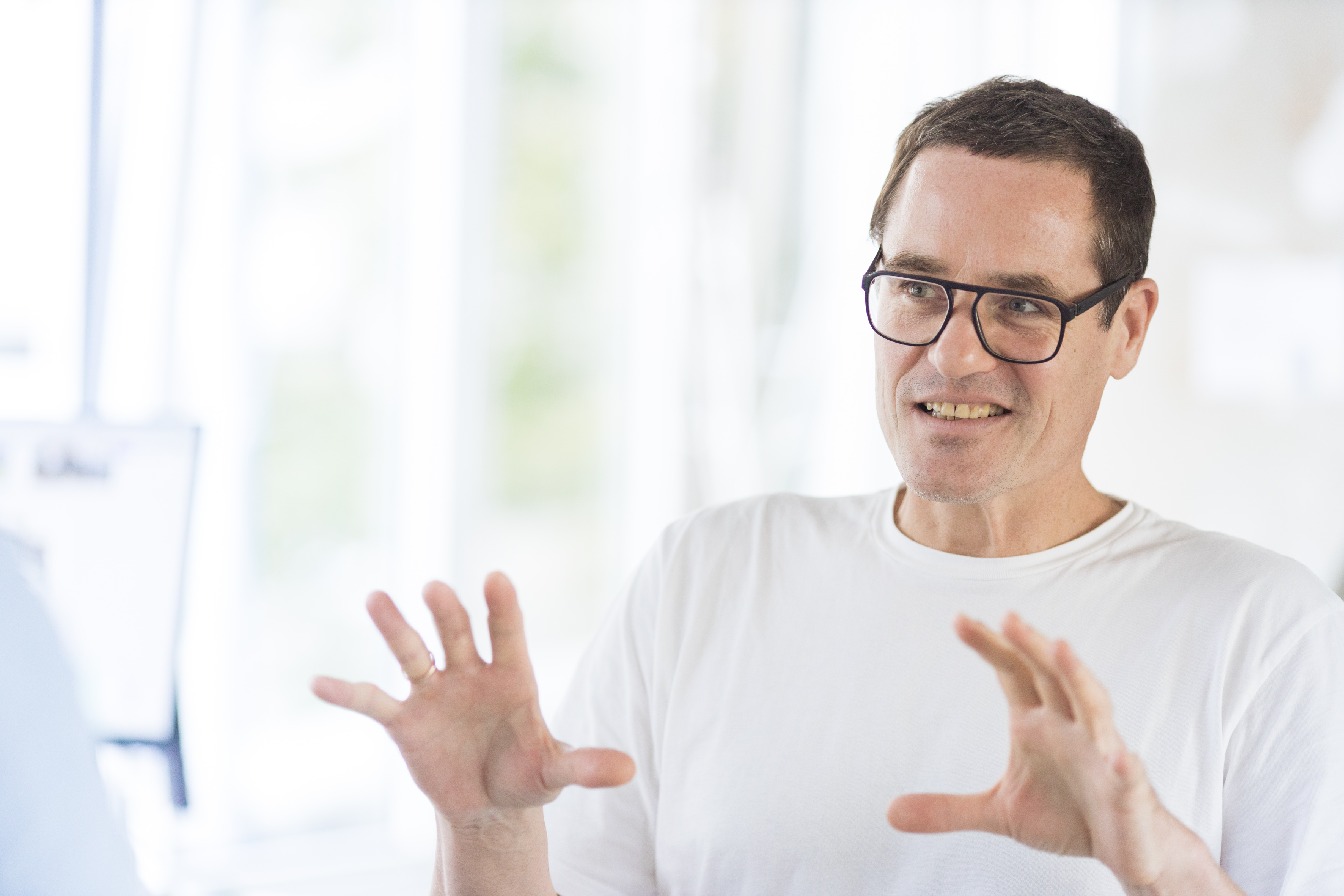 Software developer Klaus wears a white t-shirt and gestures towards the camera