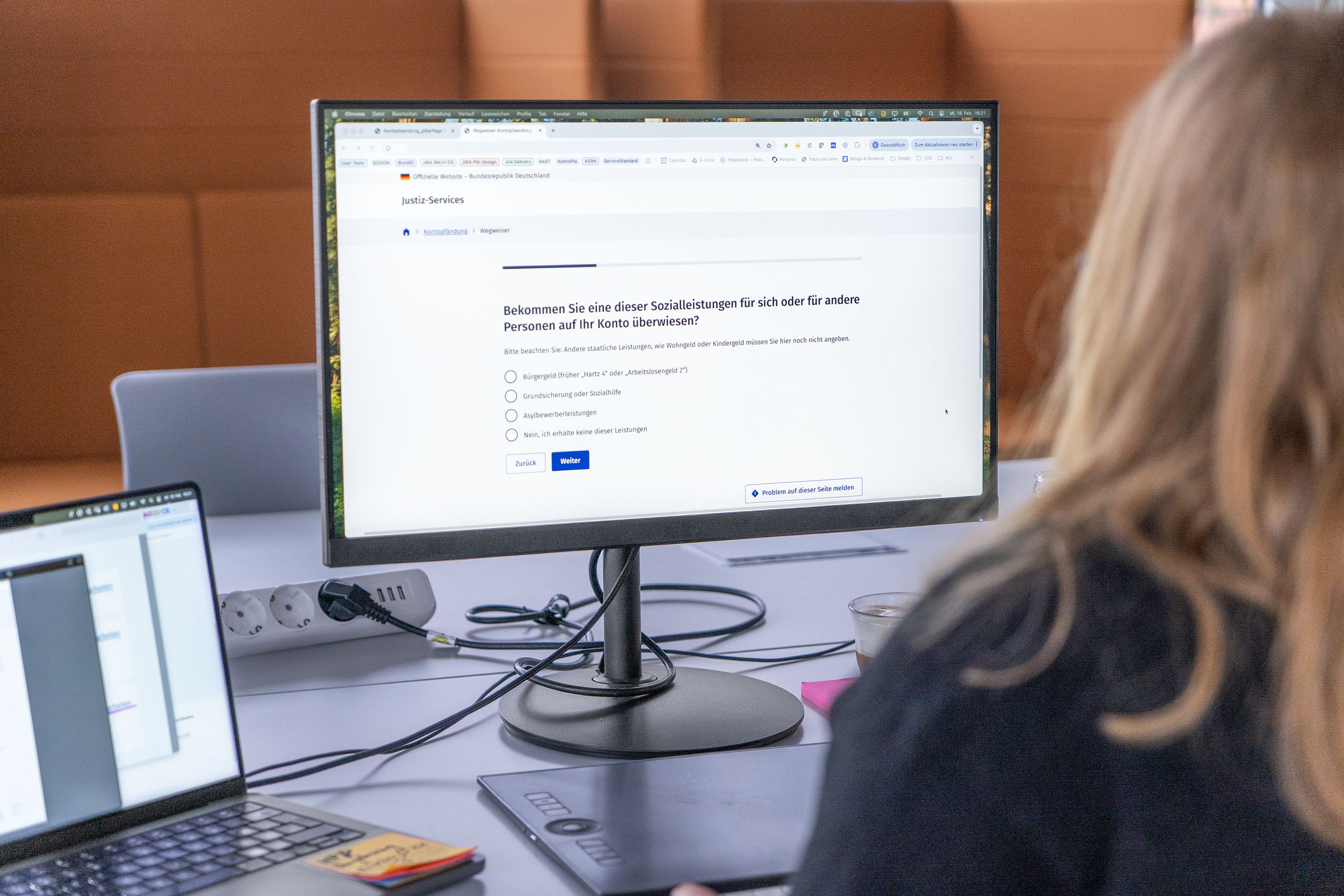 Person vor einem Computermonitor sitzend, der ein digitales Justizformular zeigt und eine Frage zum Erhalt von Sozialleistungen stellt – mit 4 unterschiedlichen Antwortmöglichkeiten