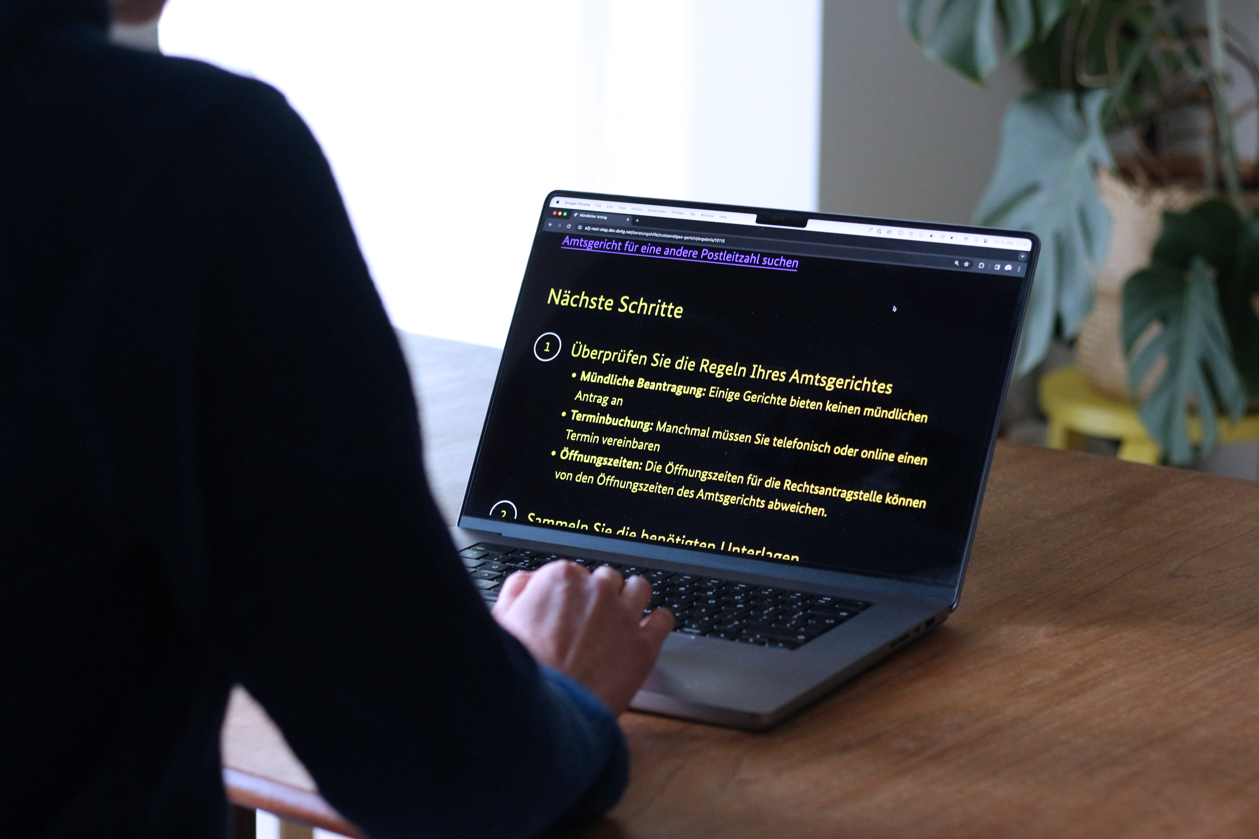 Person an einem Tisch mit Laptop-Computer auf dem stark vergrößert gelb auf schwarz eine Liste zu Amtsgerichtsbeantragungen zu sehen sind