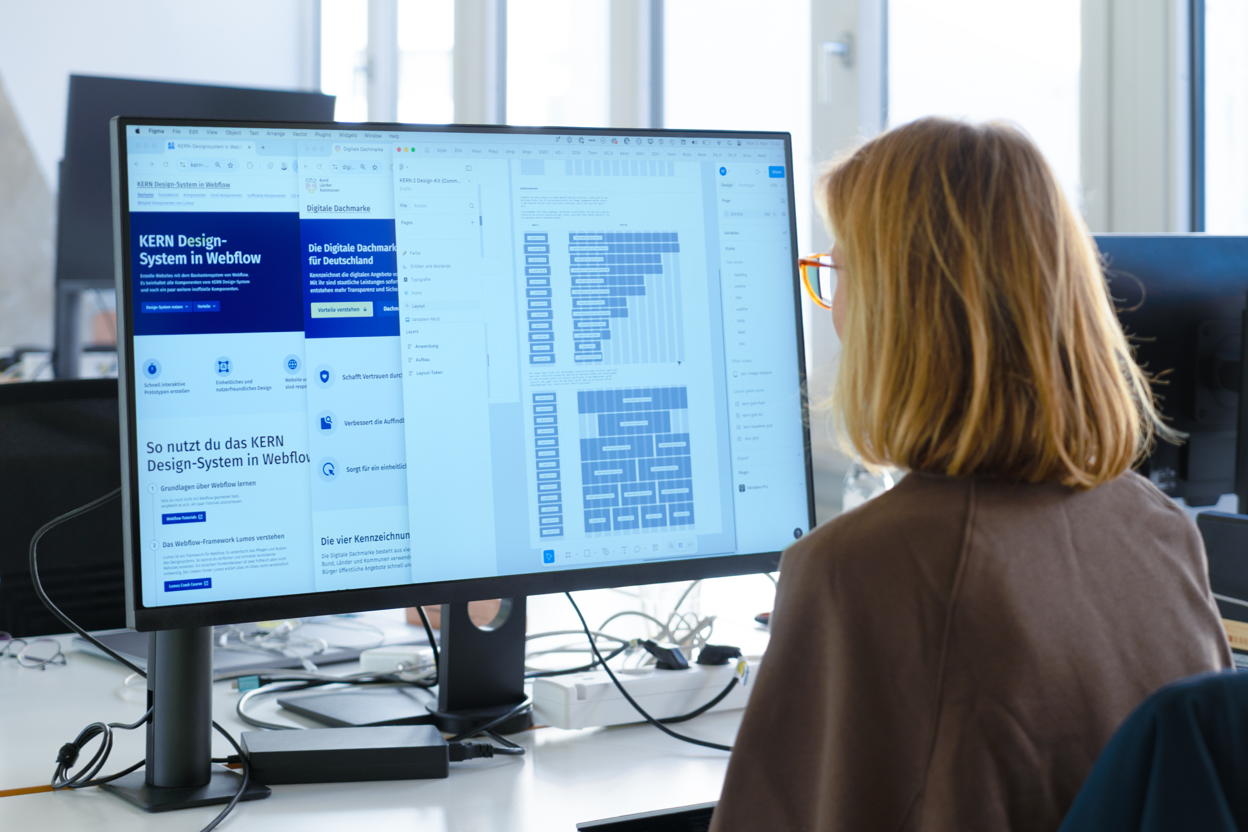 Eine Person sitzt vor einem großen Computerbildschirm, der verschiedene Fenster zeigt: mit dem KERN Designsystem, der Digitalen Dachmarke und einem Spaltensystem