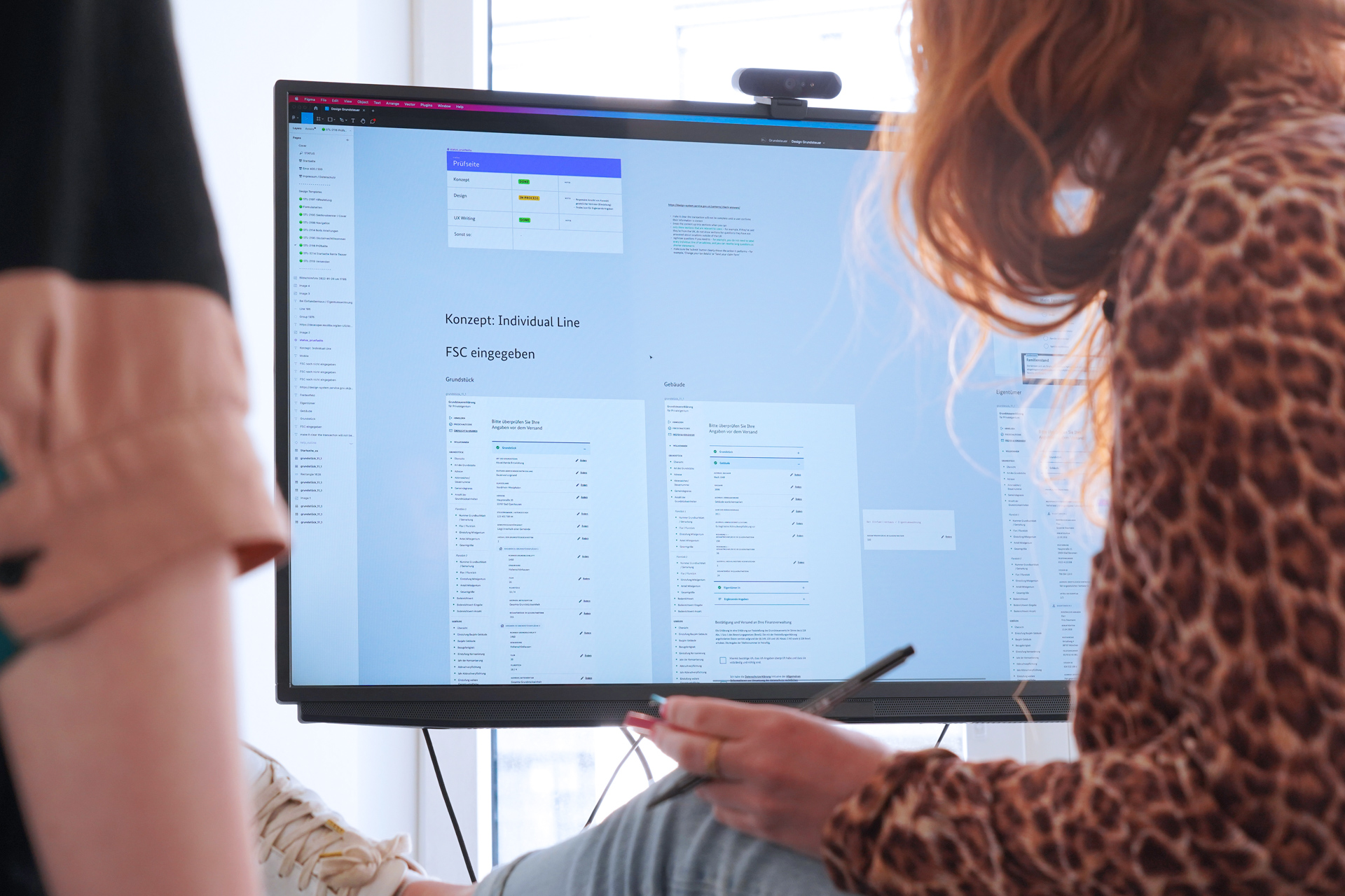 Zwei Personen mit Klebezetteln und Stiften in der Hand schauen auf einen großen Bildschirm, der verschiedene Layouts von Webseiten zeigt