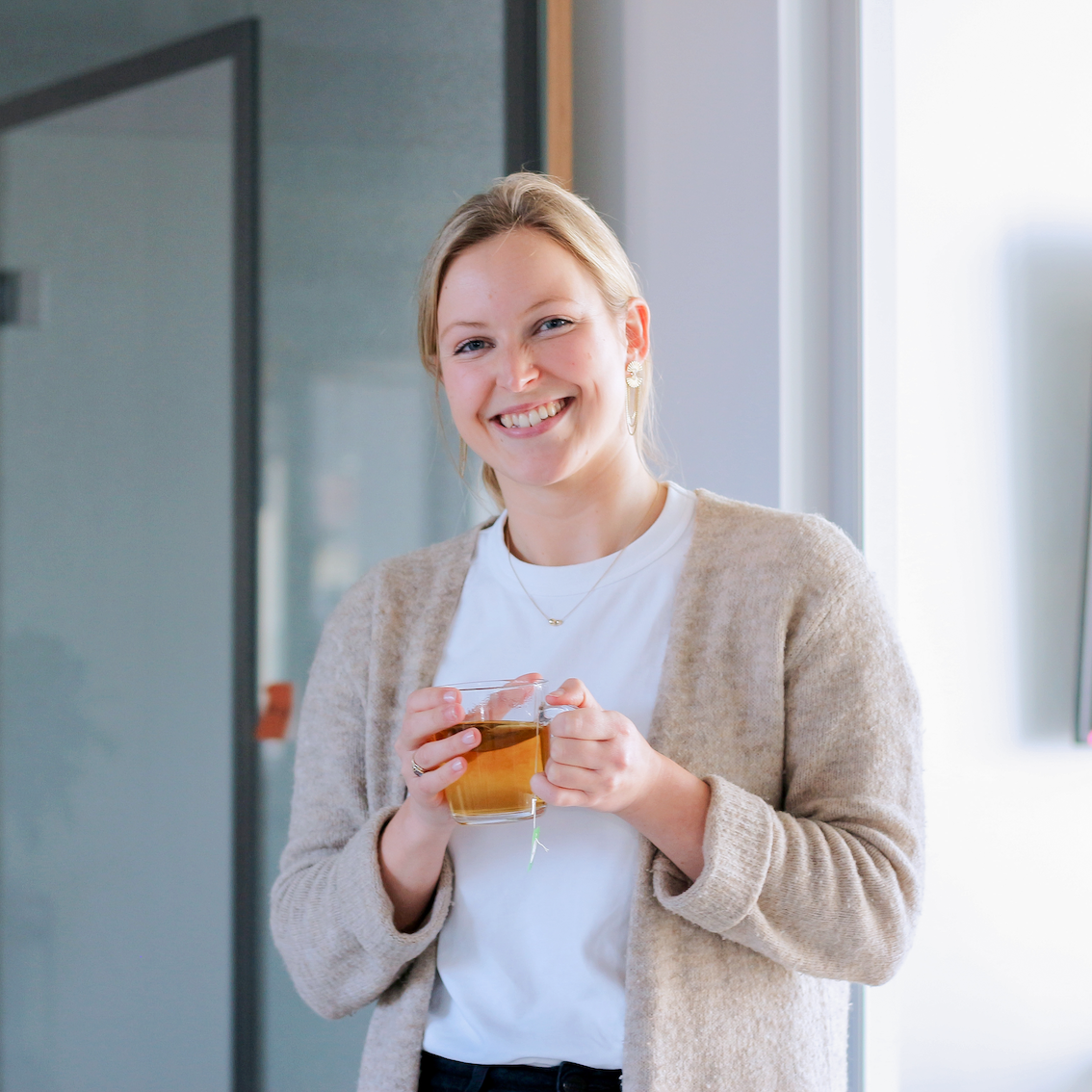 Annemie steht mit einer Tasse im Büro des DigitalService un dblickt lächelnd in die Kamera