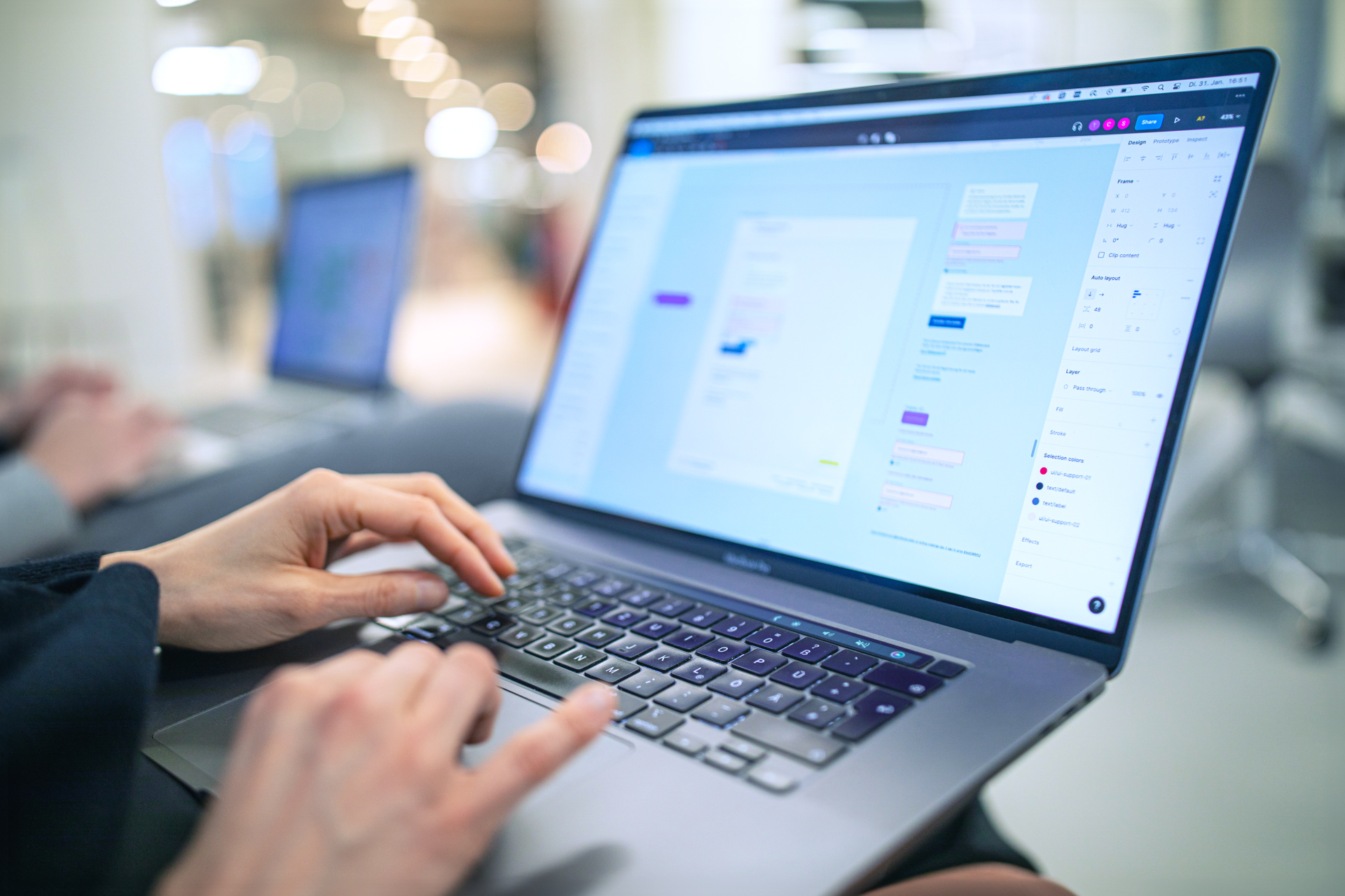 Im Fokus ist ein aufgeklapptes Laptop, an dem eine Person arbeitet, deren Hände zu sehen sind