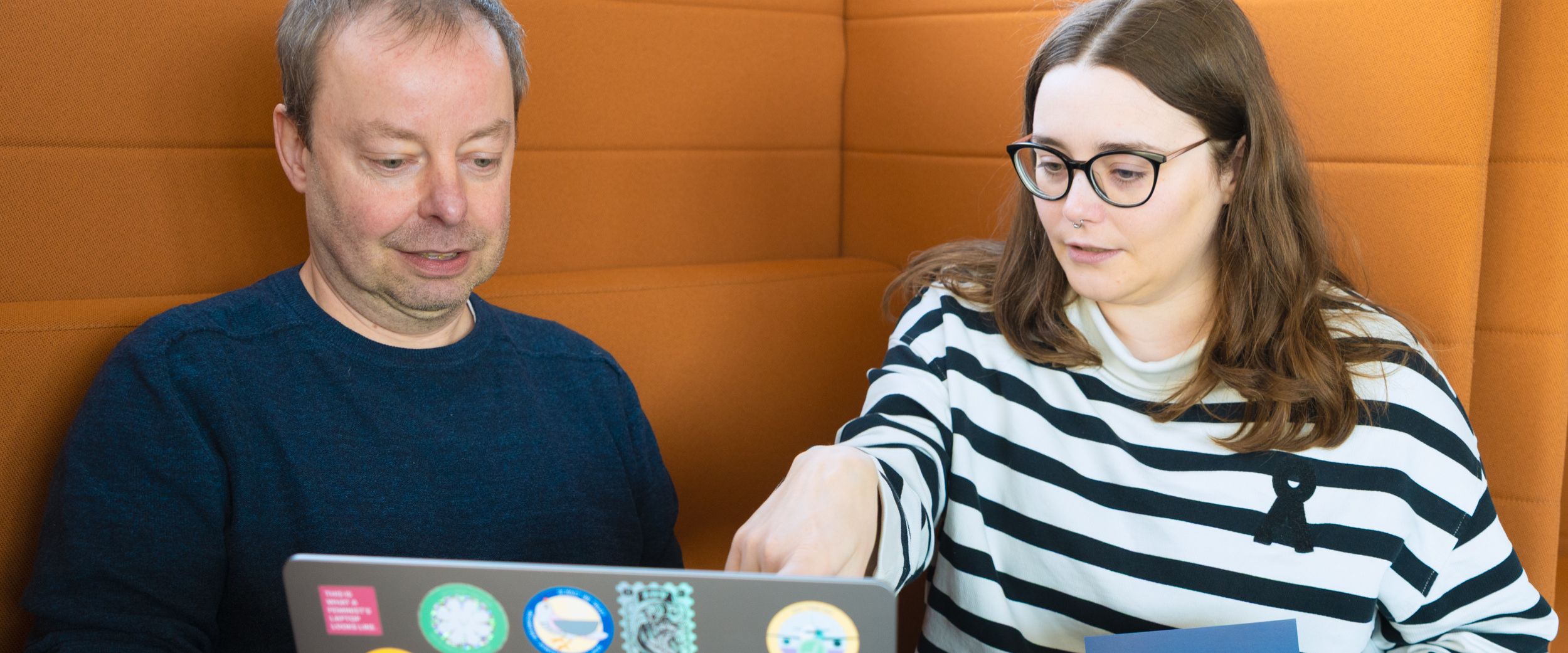 Authors Alisa Sauer and Torsten Elsner are sitting in a seating area, looking at the screen of an open laptop.