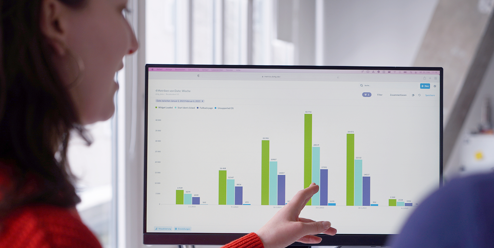Eine Person deutet auf ein Blockdiagramm auf einem Bildschirm und spricht dabei mit einer weiteren Person.