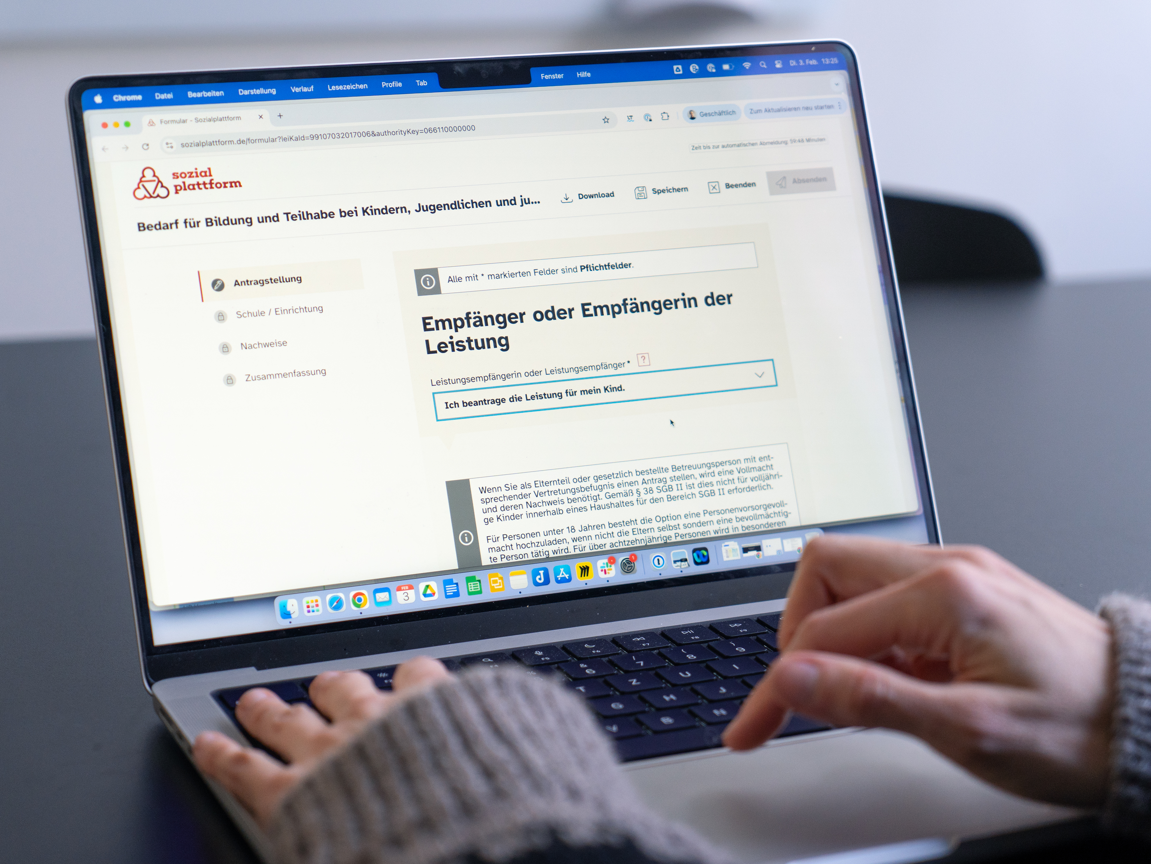 Nahaufnahme einer Person, die an einem Laptop ein Online-Formular der Sozialplattform ausfüllt. Auf dem Bildschirm ist der Antrag für „Bedarf für Bildung und Teilhabe“ zu sehen, konkret der Bereich „Empfänger oder Empfängerin der Leistung“.