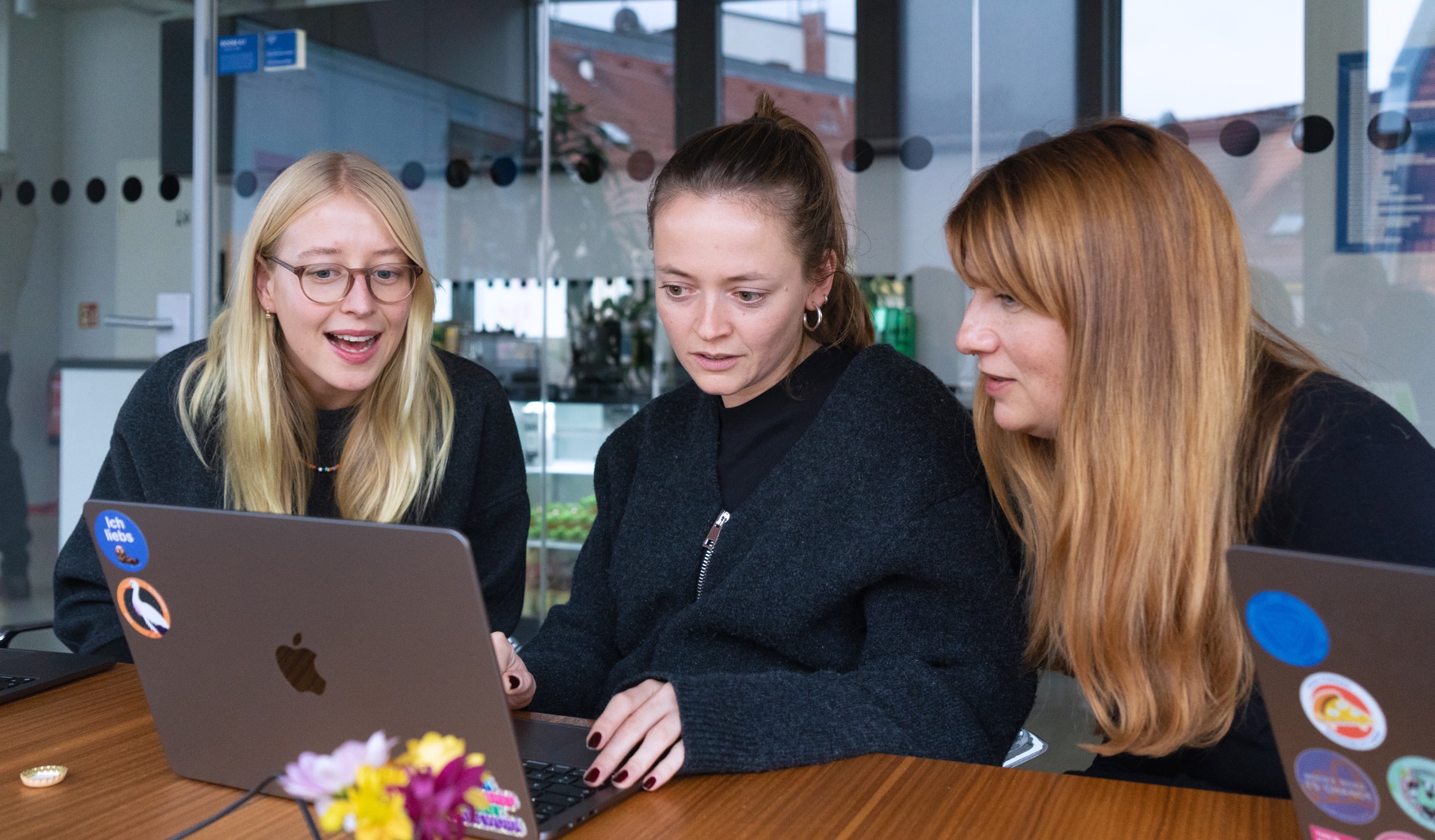 Drei User Researcher:innen sitzen gemeinsam in einem Büro an einem Tisch und schauen in ein Laptop, sie diskutieren