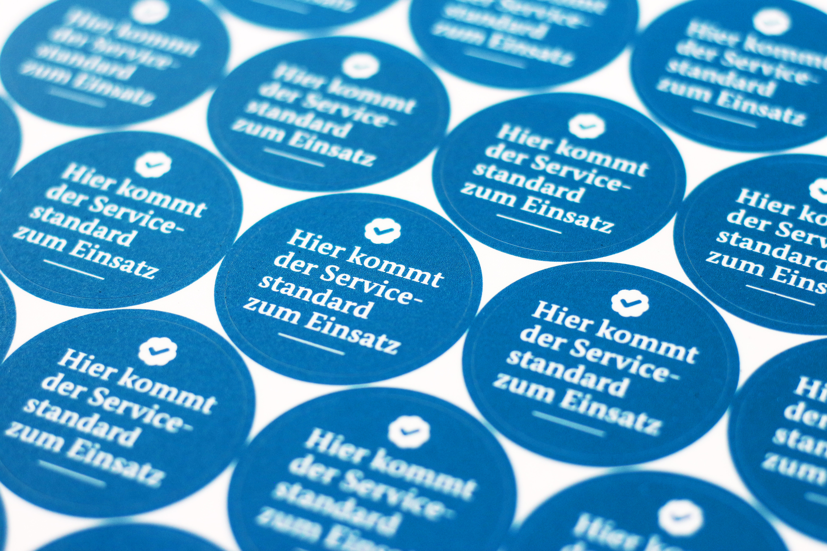 Ein Blatt mit einem Dutzend kreisförmiger Aufkleber mit der Satz: „Hier kommt der Servicestandard zum Einsatz“