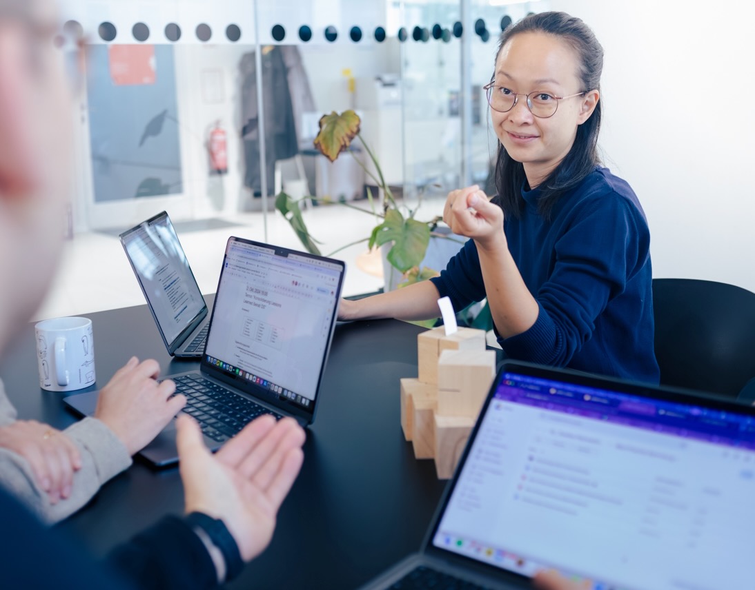 A DigitalService employee is sitting at a table talking to two colleagues. In front of her and the others are open laptops with visible documents and emails on the screens.