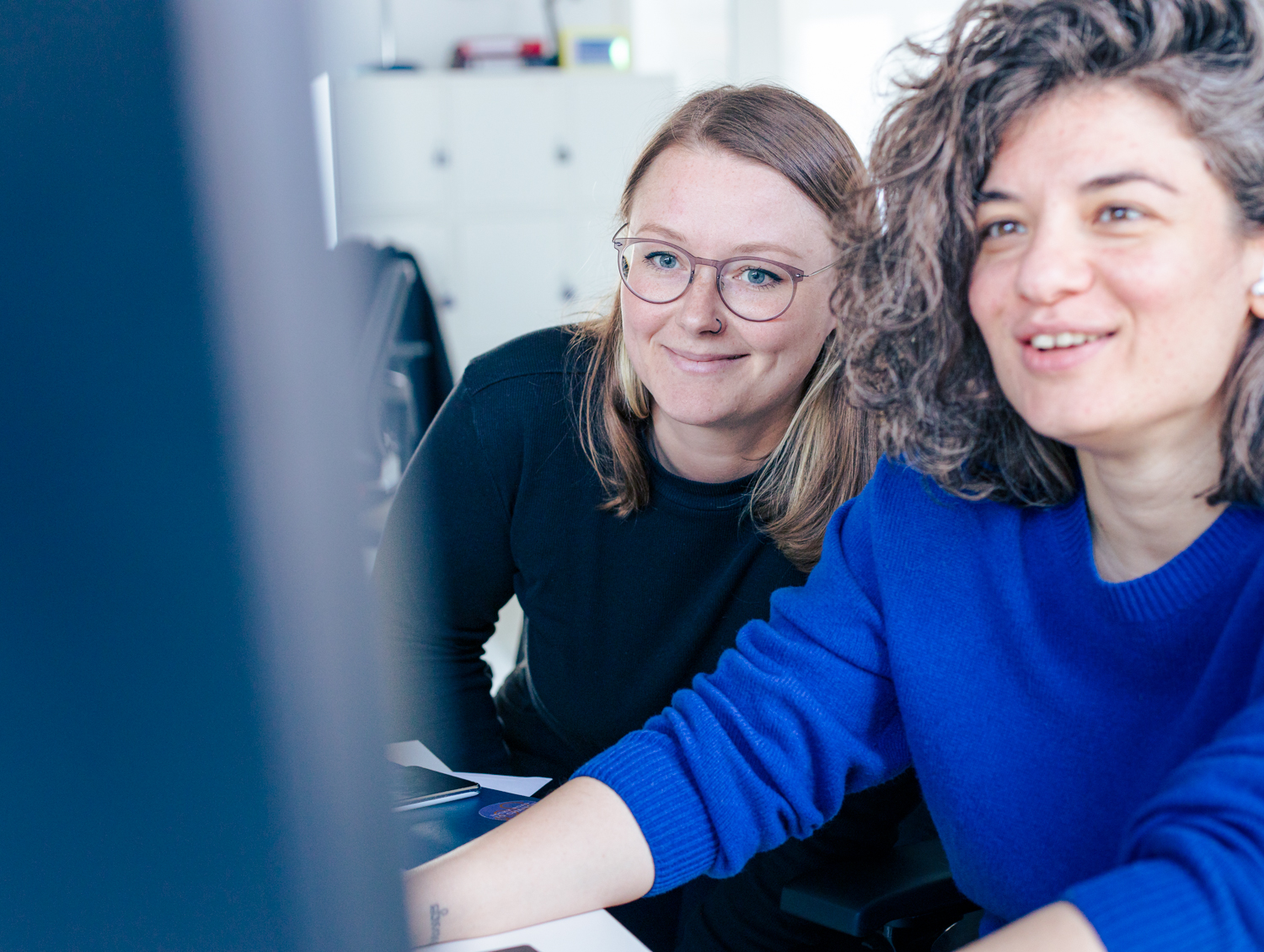 Zwei Mitarbeitende des DigitalService sitzen lächelnd gemeinsam vor einem großen Computerbildschirm und schauen sich etwas an