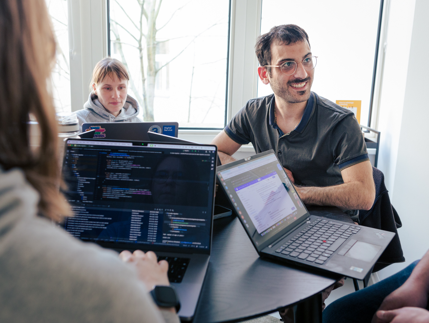 DigitalService employees sit together at a table with their laptops open and work while exchanging ideas with each other.